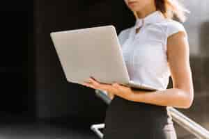 Free photo mid section of a young businesswoman holding laptop at outdoors