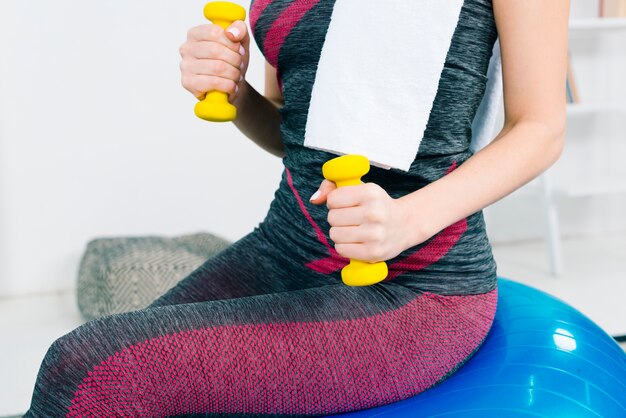 Mid section of young woman exercising with yellow dumbbells