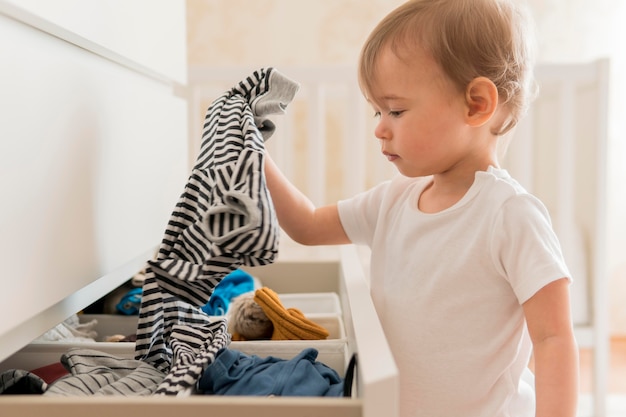 ミッドショットの赤ちゃんが引き出しから服を着て