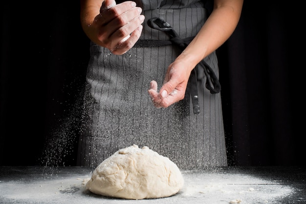 Mid shot baker pouring flour over dough