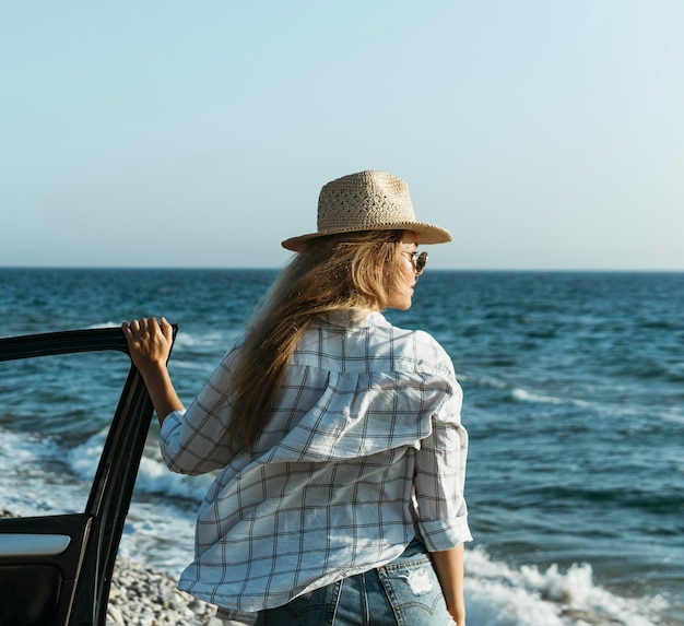 Mid shot blonde woman looking at sea by car