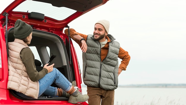 Mid shot boyfriend standing near girlfriend sitting in trunk