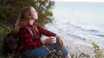 Free photo mid shot brown haired woman sitting on ground looking at sea