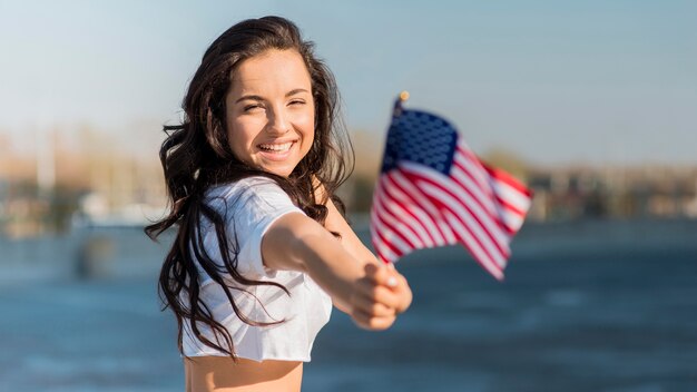 Mid shot brunette woman holding 2 usa flags near lake