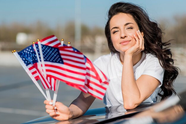 Mid shot brunette woman holding usa flags on car