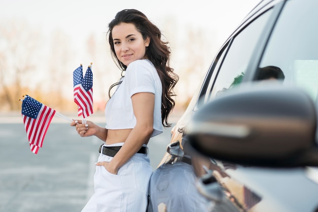 車の近くにアメリカのフラグを保持しているミッドショットブルネットの女性