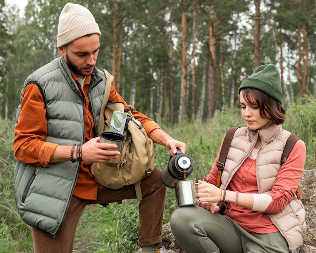 Mid shot couple pouring hot drink in nature