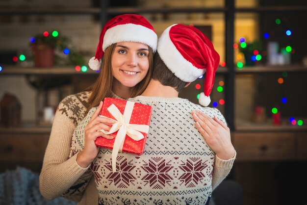 Mid shot couple wearing santa hats hugging eachother