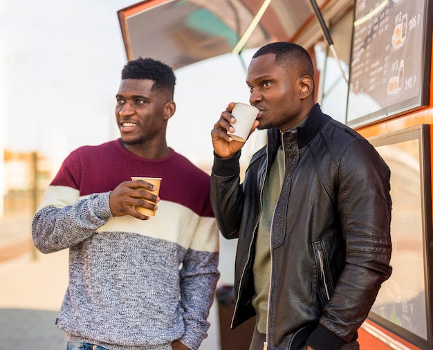 Mid shot friends enjoying coffee near food truck