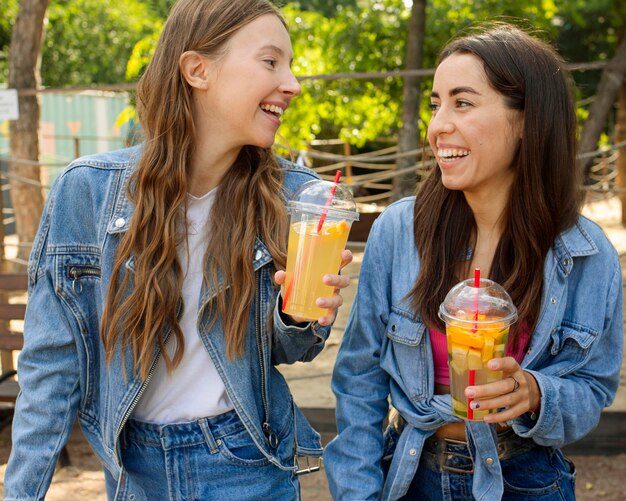 Mid shot friends holding fresh juice and laughing