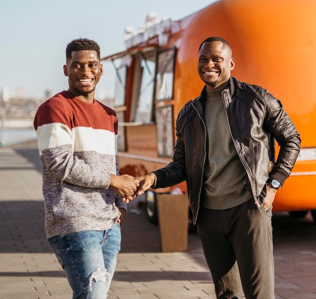 Mid shot friends shaking hands in front of food truck