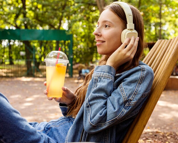 フレッシュジュースを飲むヘッドフォンでミディアムショットの女の子