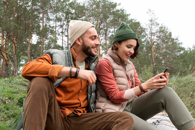 Mid shot happy couple sitting on grass and looking at phone