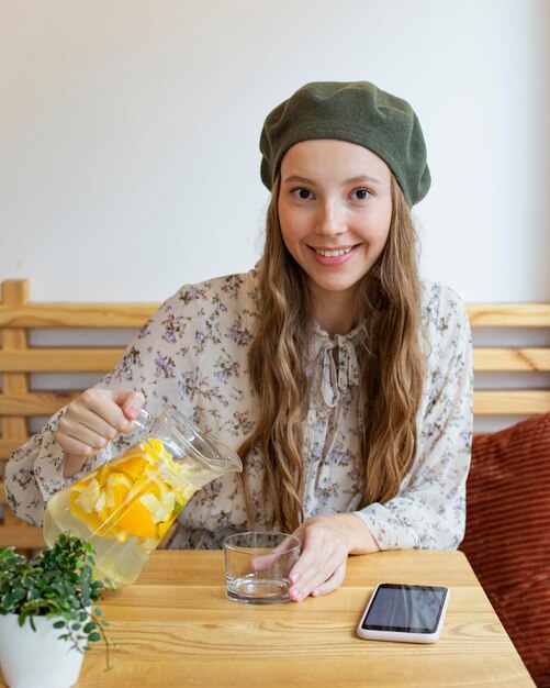 Donna felice del colpo metà che si siede al tavolo e che versa la limonata