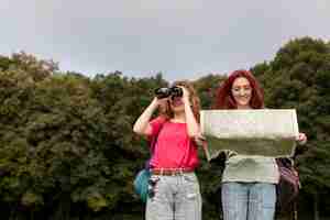 Free photo mid shot happy women with binoculars and map in nature