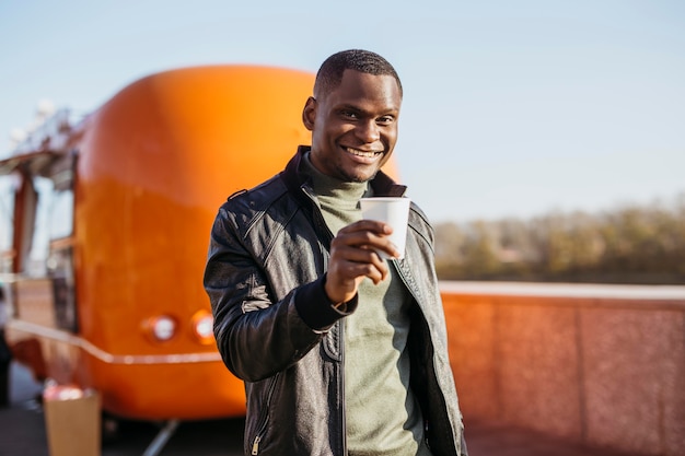 Mid shot male holding coffee cup in front of food truck