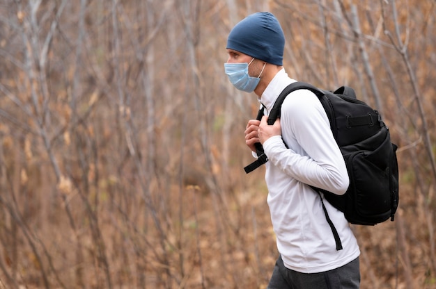 Mid shot male with face mask and backpack in the woods