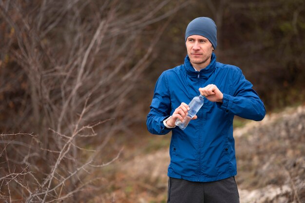 Mid shot man holding bottle of water in nature