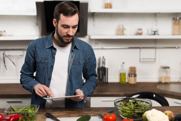 Mid shot man holding tablet in kitchen