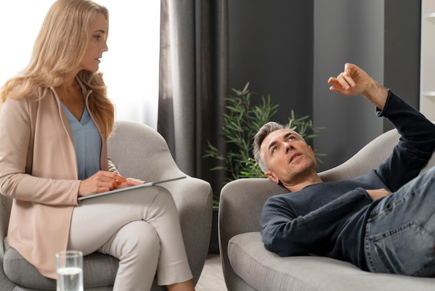 Foto gratuita uomo a metà tiro posa sul divano nell'armadietto della terapia vicino al consulente