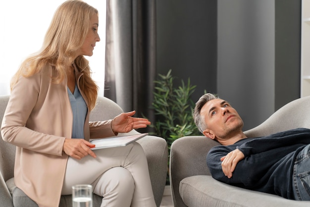 Foto gratuita uomo del colpo medio che pone sul divano nell'armadietto della terapia vicino al consulente donna