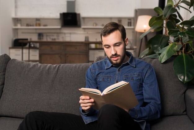 Mid shot man sitting on couch and reading book