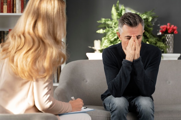 Free photo mid shot man sitting on couch in therapy cabinet near therapist