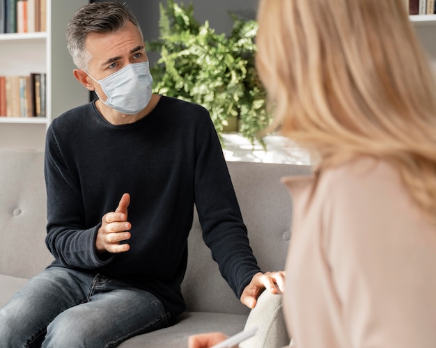 Foto gratuita uomo a metà tiro che parla al terapista che indossa la maschera