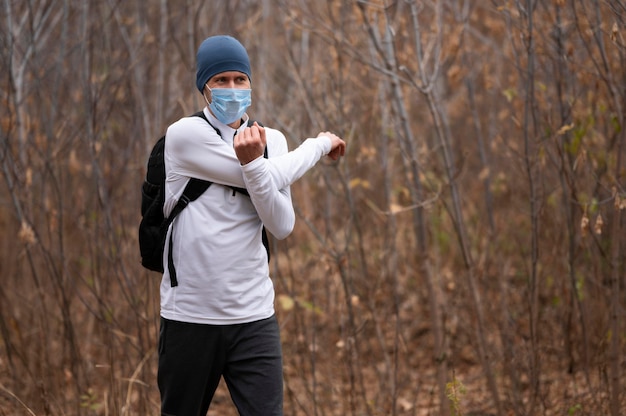 Free photo mid shot man with face mask in the woods  stretching arms