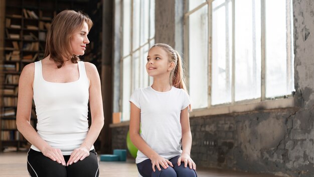 Mid shot mom and girl sitting on yoga mat