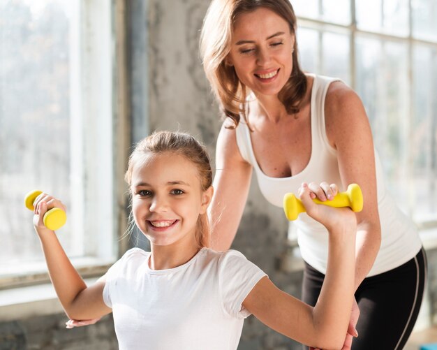 Mid shot mother helping daughter holding weights