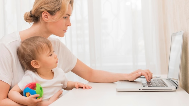 Free photo mid shot mother holding baby staying at desk