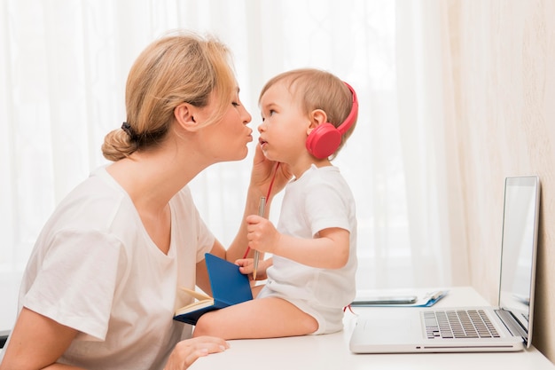 Free photo mid shot mother kissing baby on desk with headphones