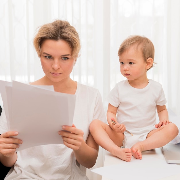 Free photo mid shot mother looking in papers and baby on desk