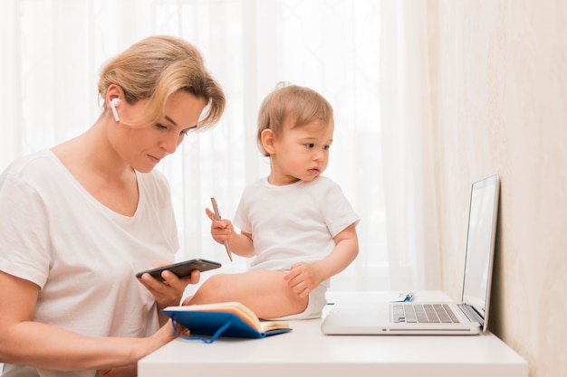 Mid shot mother looking at phone and baby on desk