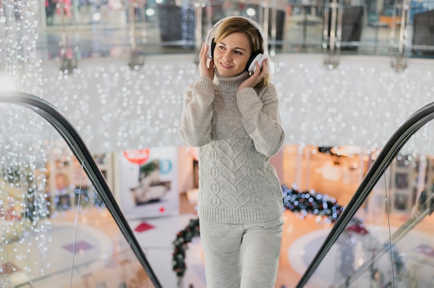 Mid shot smiling woman holding headphones on head on escalator