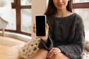 Free photo mid shot woman in cozy clothes holding nlank phone