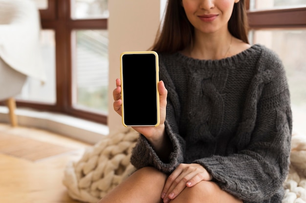 Mid shot woman in cozy clothes holding nlank phone