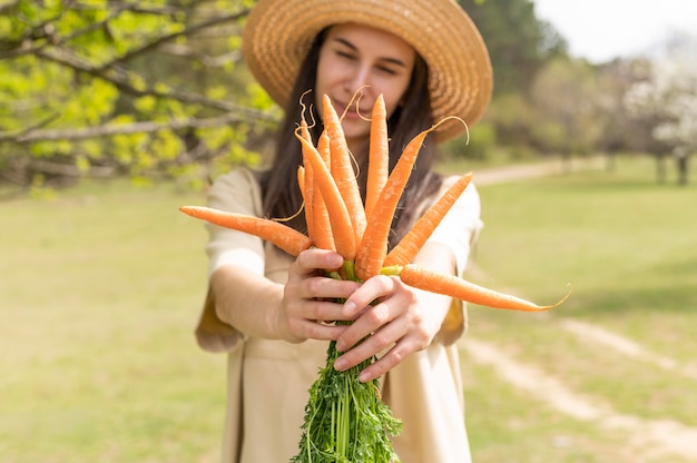 Free photo mid shot woman holding carrots outside