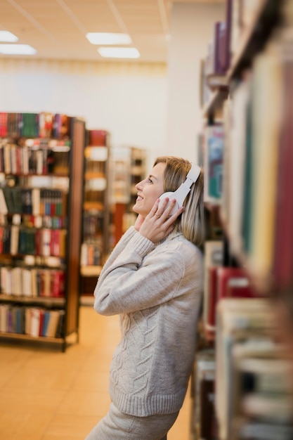 Foto gratuita metà di cuffie della tenuta della donna del colpo sullo scaffale per libri vicino capo