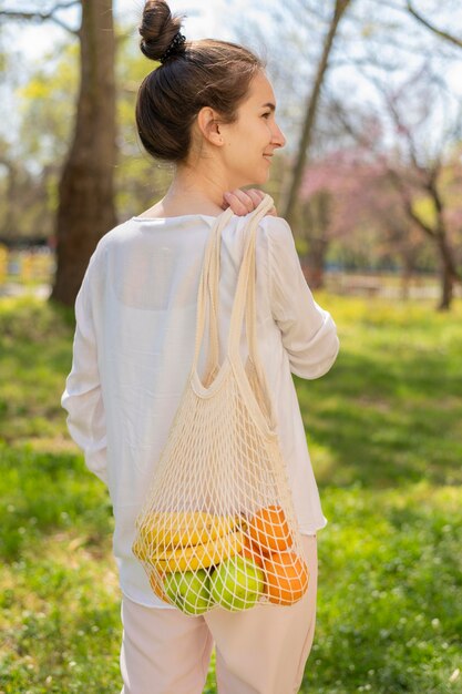 Mid shot woman holding reusable bag with food in nature