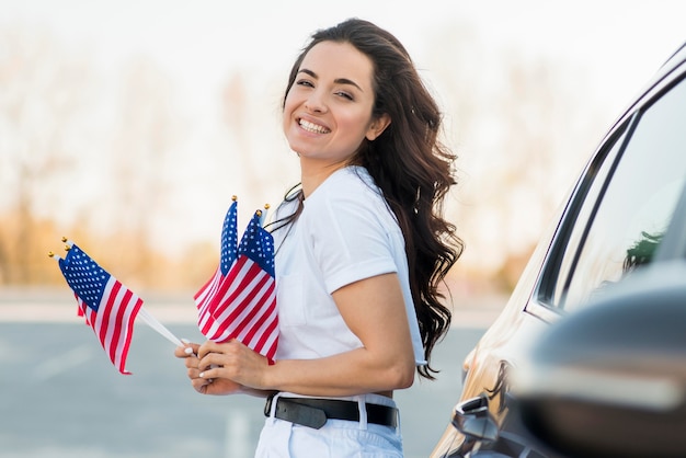 Foto gratuita la metà di donna del colpo che tiene le bandiere degli sua si avvicina all'automobile