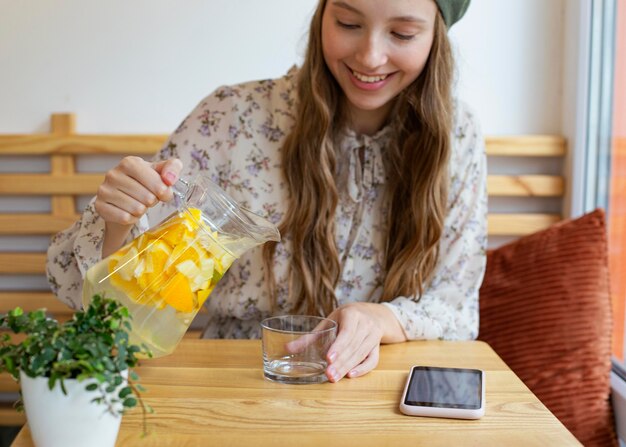 テーブルに座ってレモネードを注ぐミディアムショットの女性