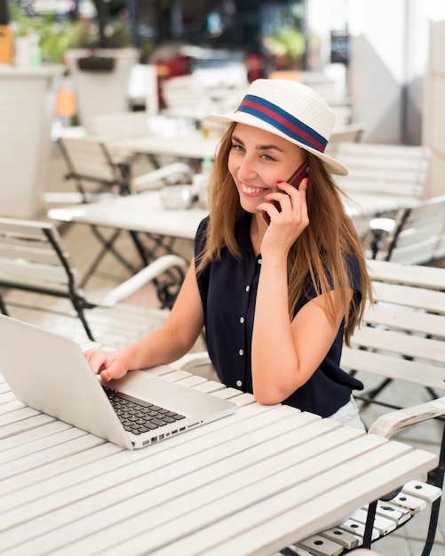 Mid shot woman at table talking on phone and using laptop