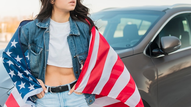 車の近くの大きなアメリカの国旗を着て半ばショットの女性