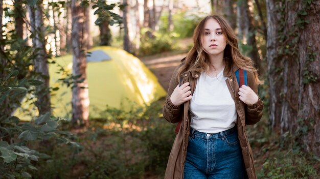 Mid shot woman with backpack in front of tent