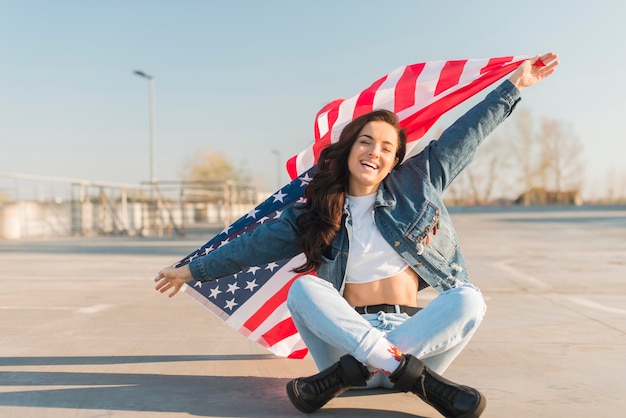 Mid shot young woman holding big usa flag sitting leg crossed