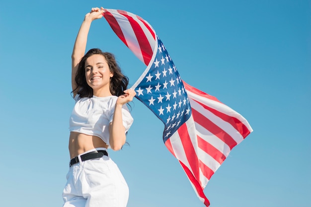 Середине выстрел молодая женщина держит большой флаг США и улыбается