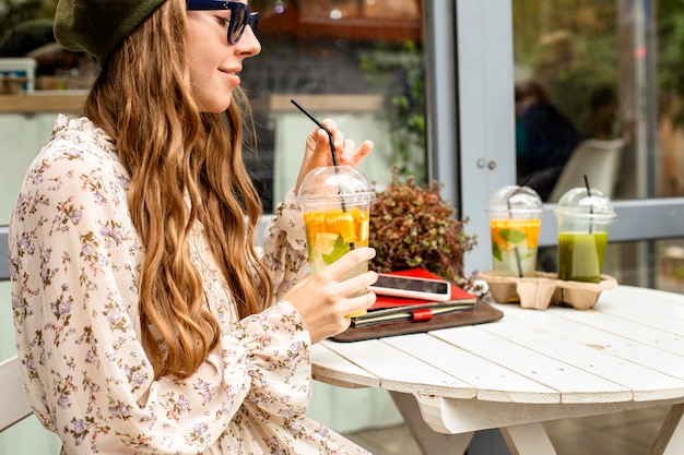 Mid shot young woman holding fresh drink and sitting at table