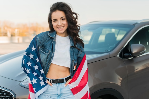 Mid shot young woman wearing big usa flag near car